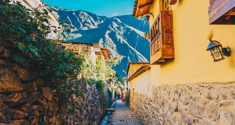 Charming cobblestone alley lined with yellow adobe houses against a dramatic mountain backdrop.