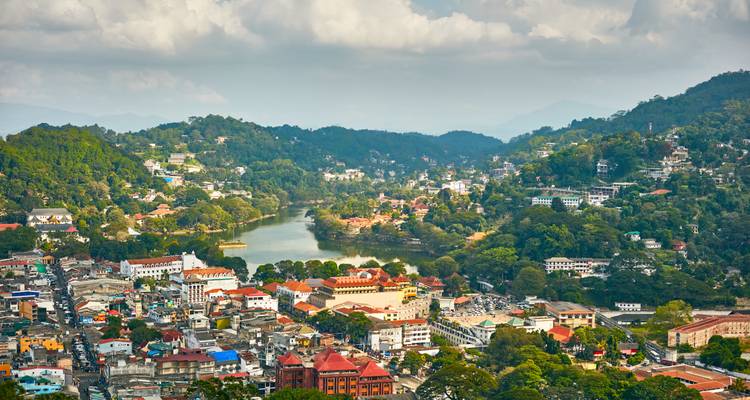Aerial panorama of Kandy city with lake at center surrounded by rolling green hills.