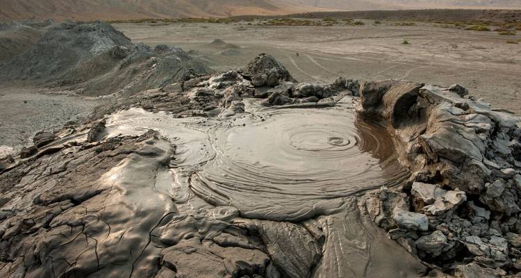 Bubbling grey mud volcano in a barren landscape.