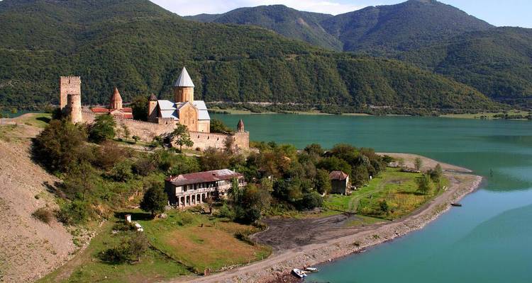 Ananuri fortress complex beside a tranquil turquoise reservoir and forested mountains.