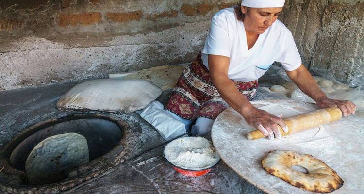 Woman prepares traditional flatbread beside a clay tandoor oven.