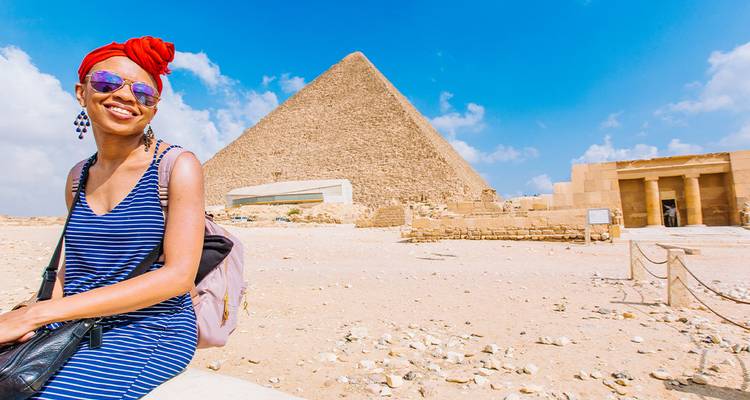 A traveler poses with the Great Pyramid of Giza rising sharply against a bright blue sky.
