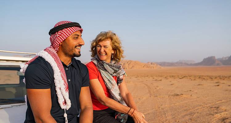 A man in traditional keffiyeh and a woman laugh together while sitting on a 4x4 in Wadi Rum’s vast desert.