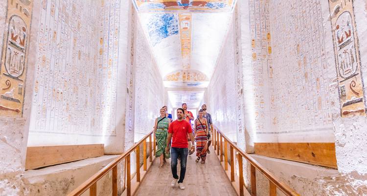 A guide leads travelers down a brightly lit corridor of an elaborately painted tomb in the Valley of the Kings.