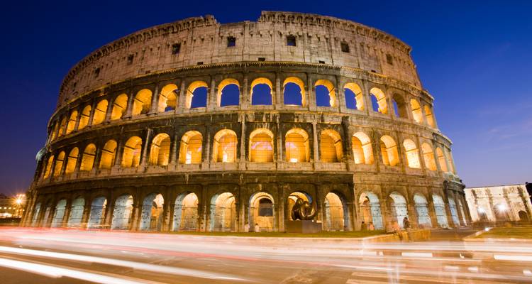 El Coliseo iluminado de noche con sendas de luz dinámica del tráfico que pasa.