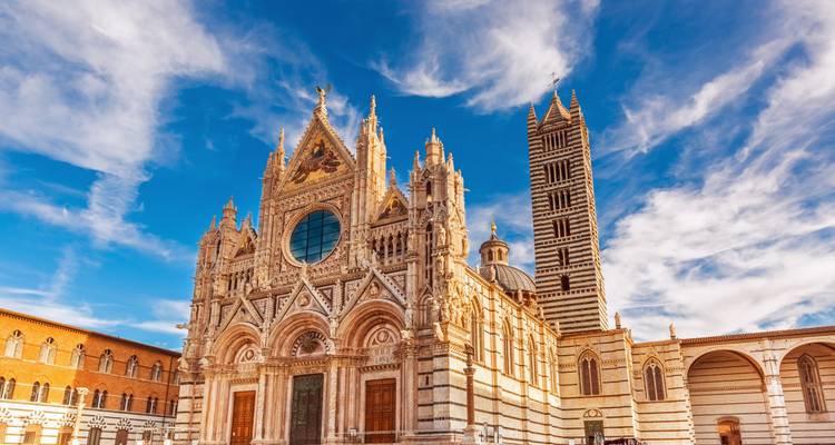 La ornada fachada de la Catedral de Siena se alza majestuosa bajo un cielo azul brillante atravesado por nubes.