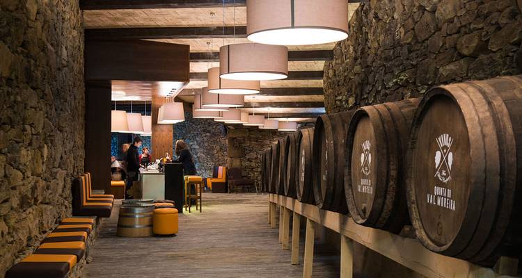 Atmospheric stone wine cellar lined with large oak barrels and soft pendant lighting where visitors taste port.