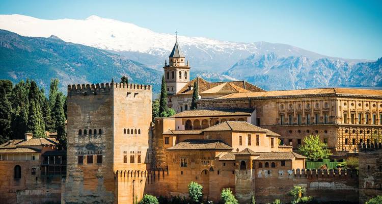 Majestic Alhambra fortress complex framed by snow-capped Sierra Nevada mountains under a clear sky.