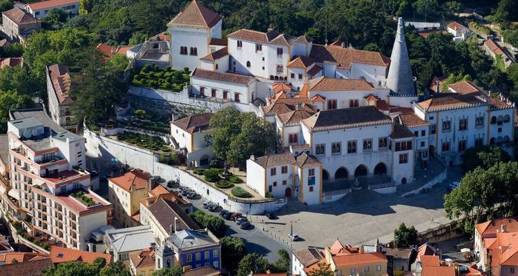 Aerial view of the white-walled Sintra National Palace and surrounding red-roofed buildings nestled among green hills.