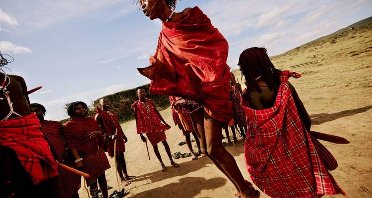 Maasai performers in red shuka jumping high during a traditional dance in open plains