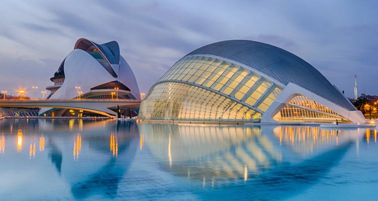 Las curvas futuristas de la Ciudad de las Artes y las Ciencias de Valencia reflejadas en una piscina color turquesa durante el atardecer.