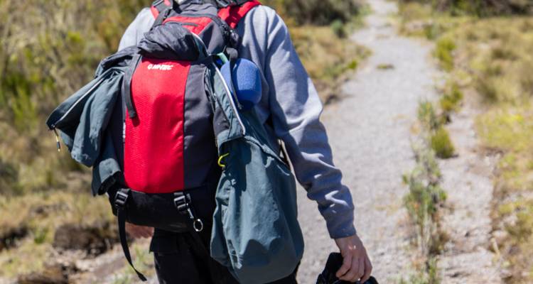 Close-up of a trekker’s backpack while walking on a rocky mountain trail.