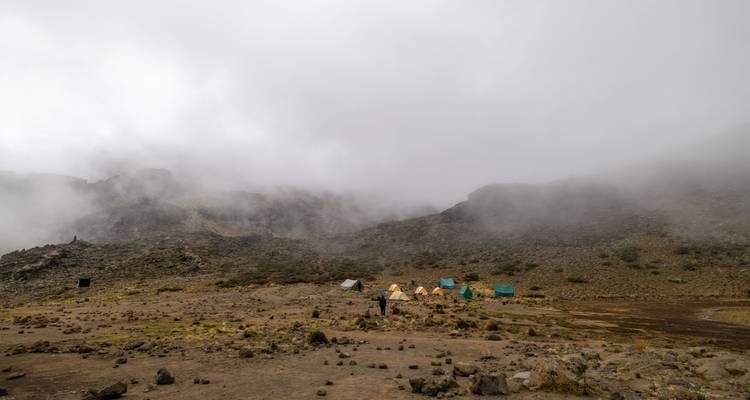 Fog-shrouded alpine campsite with scattered tents at the base of rocky cliffs.