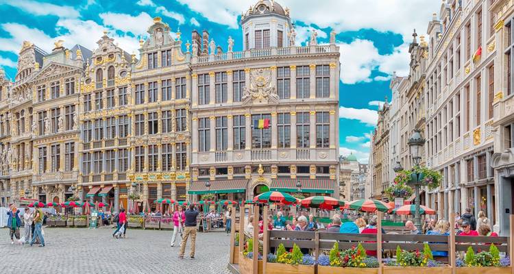 Plaza grande y vibrante con casas gremiales ornamentadas y terrazas de cafés bulliciosas bajo cielos azules.