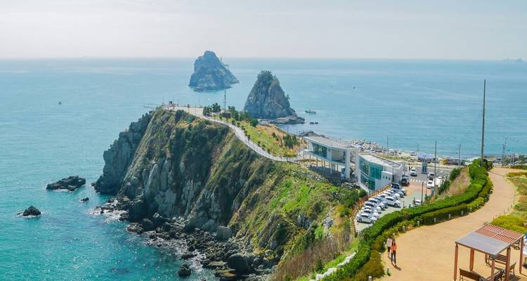 Promontorio rocoso de la costa con caminos para caminar e islotes en el mar rodeados de un tranquilo mar azul.