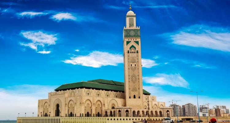 The massive Hassan II Mosque stretches along the Atlantic waterfront beneath a vivid blue sky.