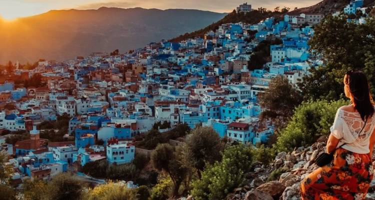 A traveller gazes over the blue-washed houses of Chefchaouen from a hillside at sunset.