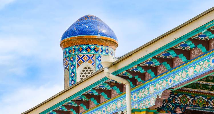Detailed blue-and-green mosaic tiles adorn a small minaret and wooden eaves against a light sky.