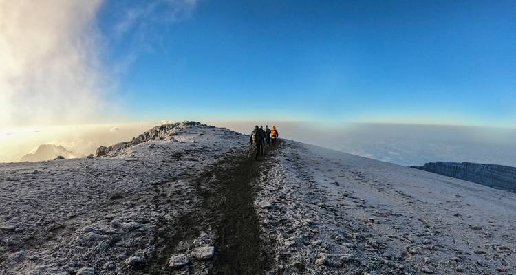 Une file de trekkeurs marchant le long d'une crête de cratère givrée sous un ciel bleu dégagé.