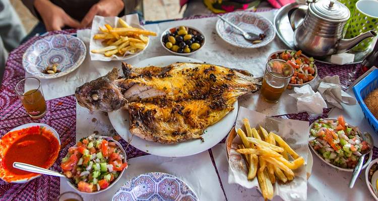 Un poisson grillé et des accompagnements généreux couvrent une table marocaine colorée prête à être partagée.