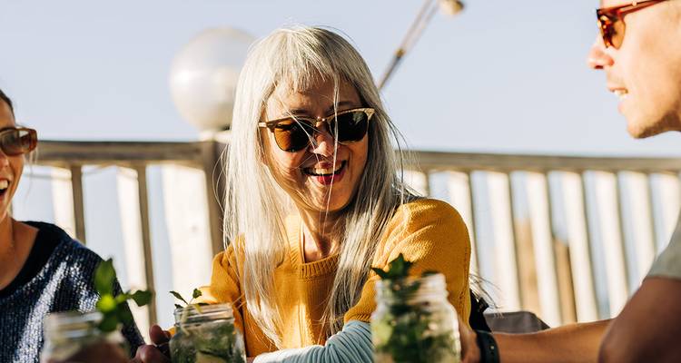 Des amis souriants savourent des boissons dans des bocaux en verre sur une terrasse ensoleillée.