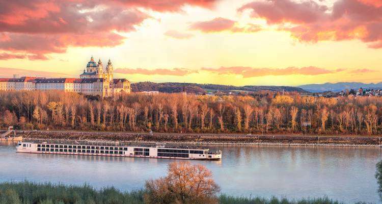 Long riverboat cruises beneath a glowing sunset opposite the grand baroque abbey set above autumn-colored forest on the Danube bank.