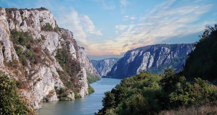 Steep limestone cliffs flank the blue Danube River in the Iron Gate Gorge at dawn.