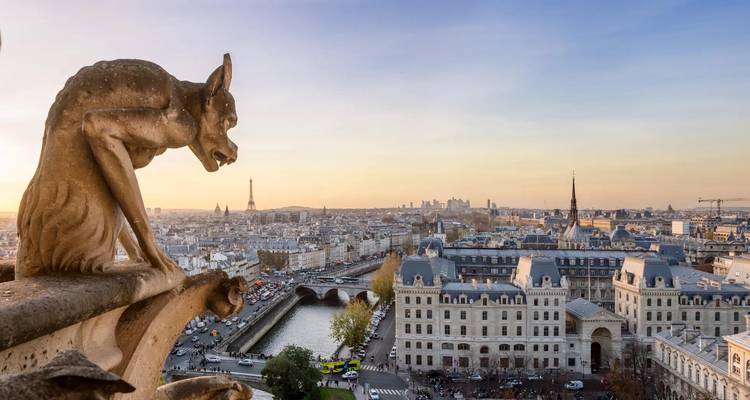 Stone gargoyle of Notre-Dame overlooks Paris rooftops and the Eiffel Tower at dusk.