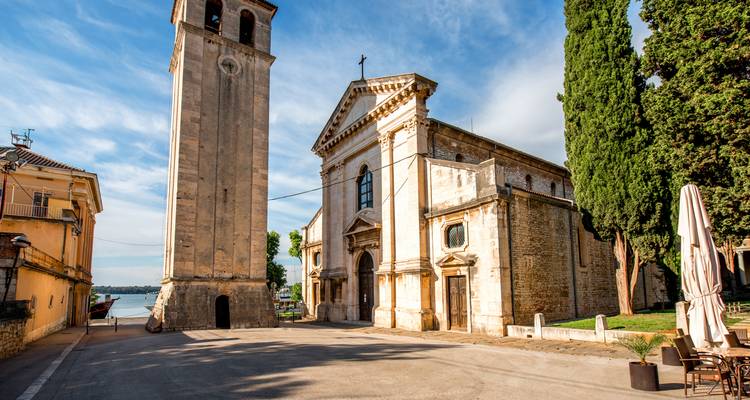 Stone church and tall bell tower overlooking a quiet coastal village street in Istria.