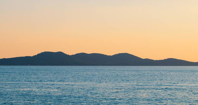 Minimalist seascape of calm Adriatic waters with distant island silhouettes at dusk.