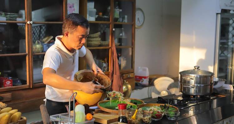Chef prepares Thai dish scooping ingredients from a hollowed pumpkin during a hands-on cooking class in a cozy kitchen.