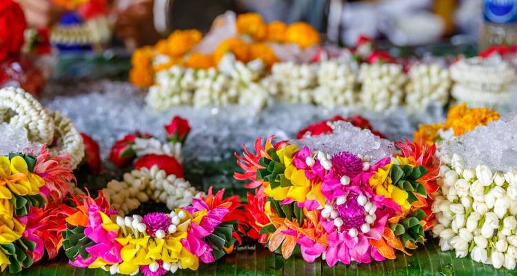Colorful garlands of fresh flowers and jasmine buds rest on crushed ice at a bustling Thai flower market.