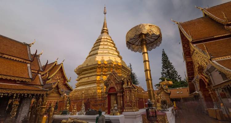 Golden stupa and ornate parasol at Wat Phra That Doi Suthep shine under dramatic cloudy skies in a temple courtyard.