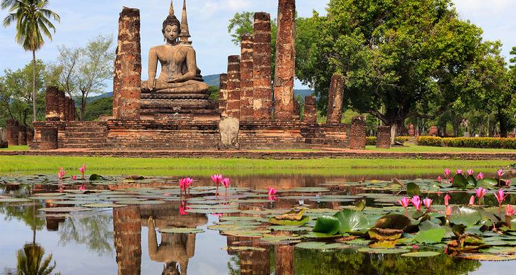 Ancient seated Buddha statue reflected in a lotus-filled pond amid brick pillars of Sukhothai Historical Park.