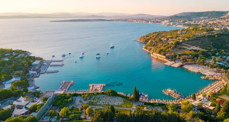 Vista aérea de la hora dorada de una bahía turquesa punteada de yates y enmarcada por colinas verdes cerca de Cesme.