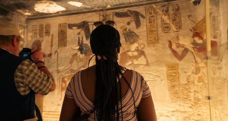 Los turistas observan coloridos murales de antiguas deidades egipcias dentro de una cámara funeraria poco iluminada.