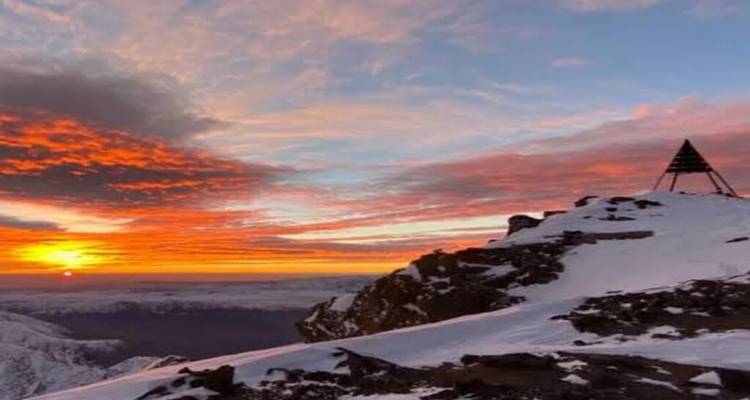 Coucher de soleil flamboyant sur une crête enneigée avec la pyramide du sommet Toubkal en silhouette.