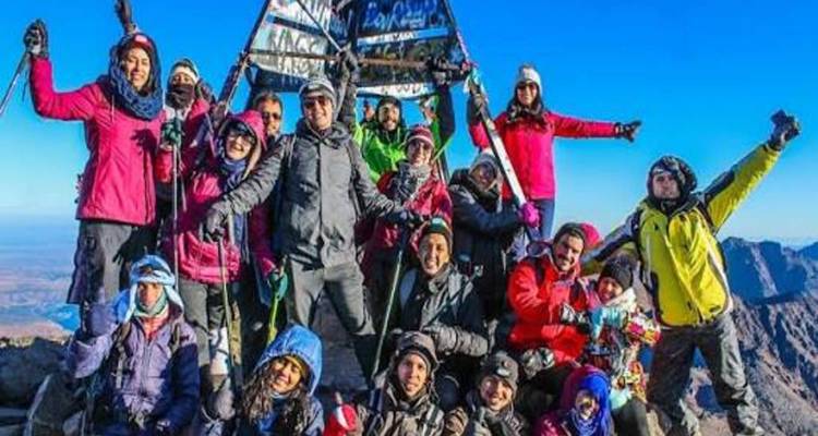 Groupe de randonneurs joyeux posant devant le marqueur du sommet du Mont Toubkal par une journée dégagée.