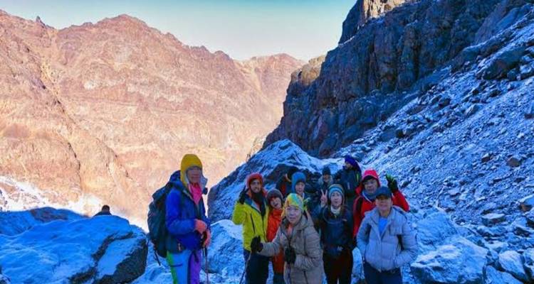 Groupe de randonneurs debout sur un sentier de montagne enneigé entre des parois rocheuses abruptes.