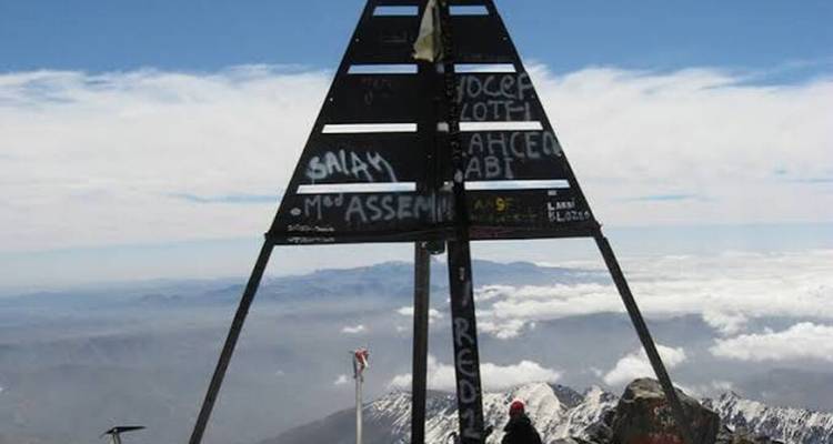 Voyageur se reposant sous la pyramide du sommet du Toubkal couverte de graffitis au-dessus de la couche nuageuse.