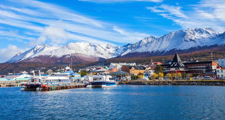 Levendige havenscène in Ushuaia met boten afgemeerd tegen een achtergrond van besneeuwde toppen onder blauwe hemels.