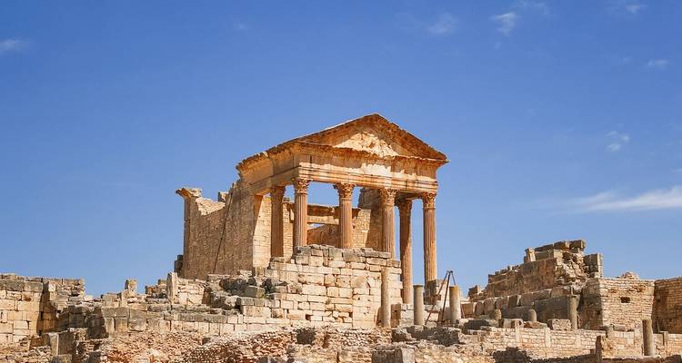 Well-preserved Roman Capitol temple ruins at Dougga standing against a bright blue sky