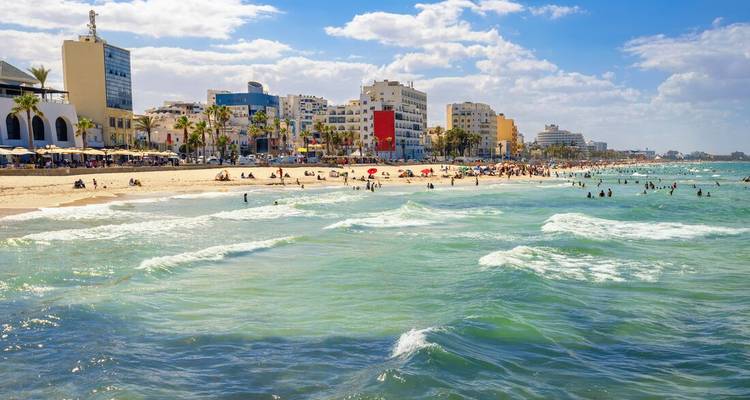Sunny beachfront cityscape of Sousse with swimmers in turquoise Mediterranean waves