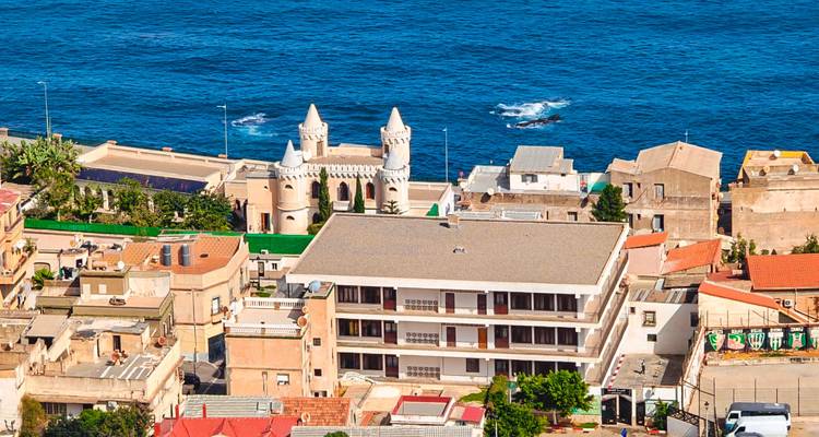 A seaside Algerian town with distinctive white towers sits perched above the deep blue Mediterranean.