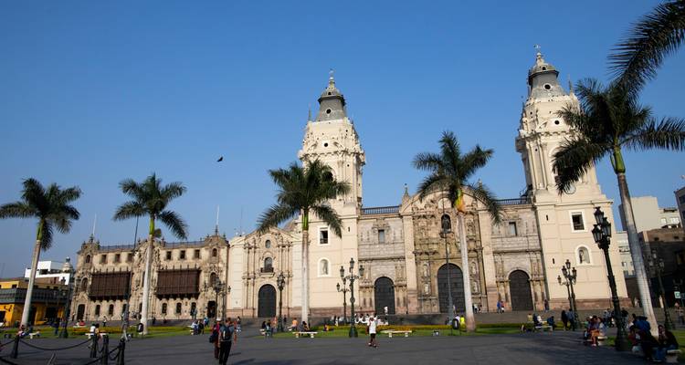 Toma aérea de la Catedral de Lima y los edificios coloniales que la rodean en la Plaza Mayor con visitantes paseando.