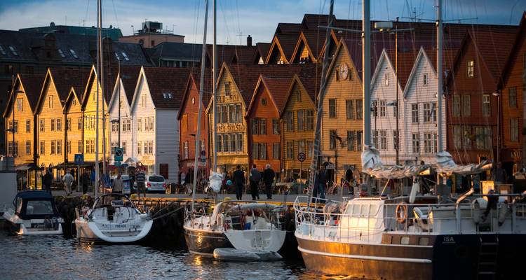 La lumière du soir illumine les entrepôts historiques de Bryggen se reflétant dans le port aux côtés des voiliers amarrés.