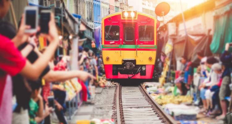 Un train rouge-jaune éclatant s'approche à travers le marché bondé de Maeklong avec des spectateurs prenant des photographies à côté des voies.