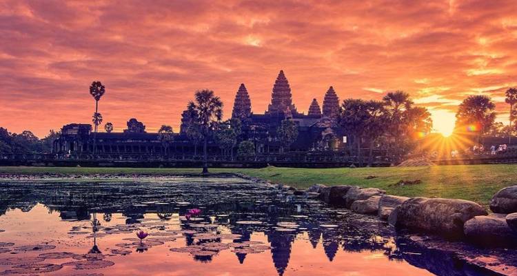 Angkor Wat se profilant sur un lever de soleil dramatique aux teintes pourpre et orange avec les reflets du bassin de lotus au premier plan.