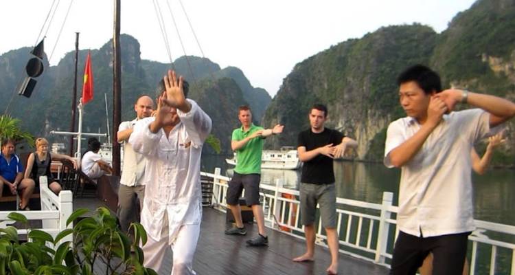 Les touristes pratiquent le tai-chi sur le pont d'un bateau au milieu des îles calcaires de karst sur une eau calme.