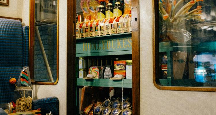 Vintage train carriage kiosk stocked with colorful sweets and drinks behind glass panels.